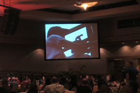 Nancie with hammer on big screen at fundraiser dinner